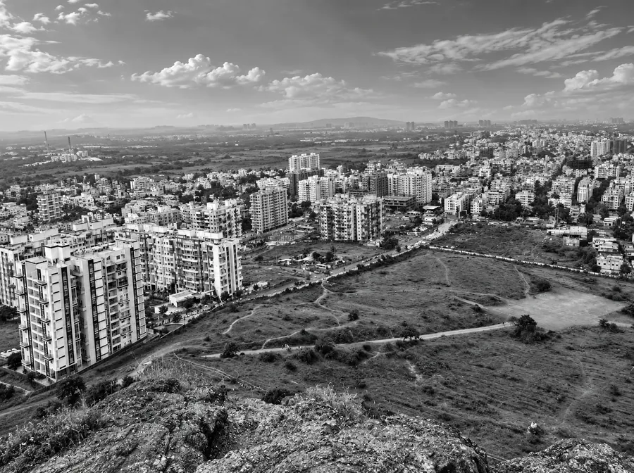 Elevated view from a rocky hilltop across apartment blocks, open scrubland and low-rise housing stretching to the horizon.