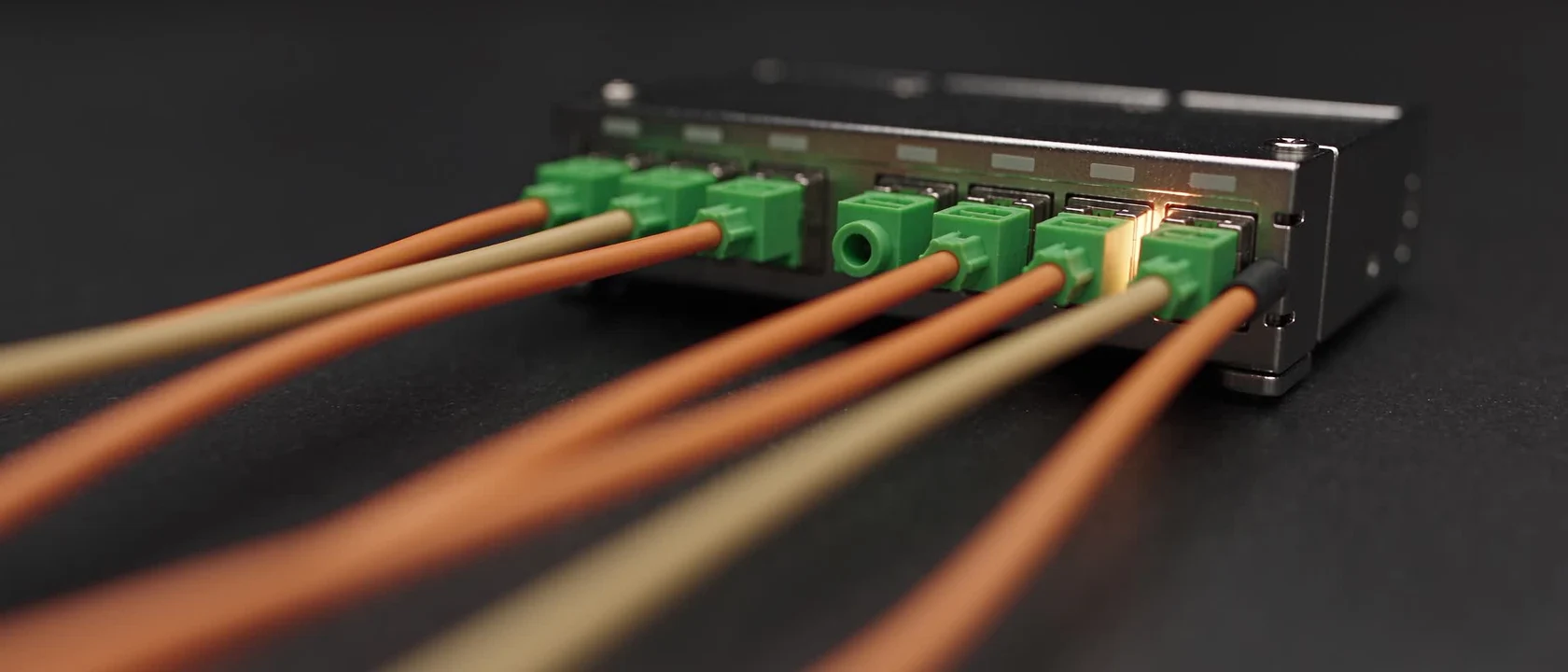 Macro fibre-optic study with orange and yellow cables and green optical connectors.