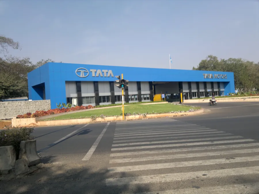 Blue and grey corporate gatehouse building with Tata Motors signage, seen across a pedestrian crossing on a wide road.